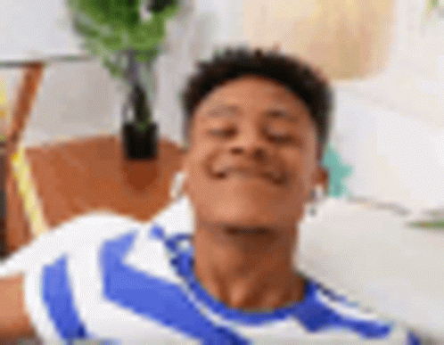 A Young Man In A Blue And White Striped Shirt Is Laying On A Couch With His Eyes Closed And Smiling . GIF