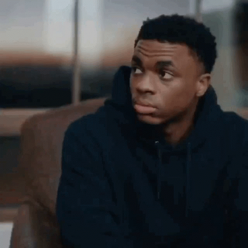 A Young Man In A Blue Hoodie Is Sitting On A Couch And Looking At The Camera . GIF