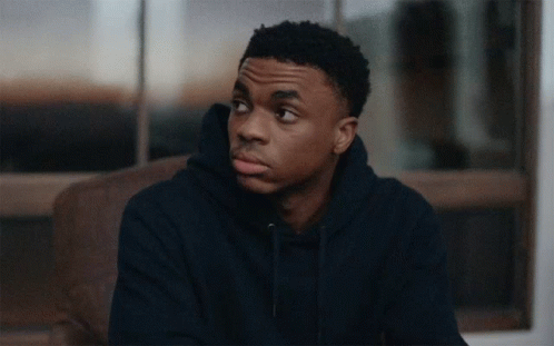 A Young Man In A Blue Hoodie Sits On A Couch Looking Out A Window GIF