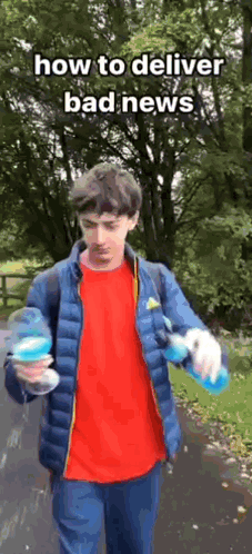a young man in a blue jacket is holding a bottle of water while walking down a road .
