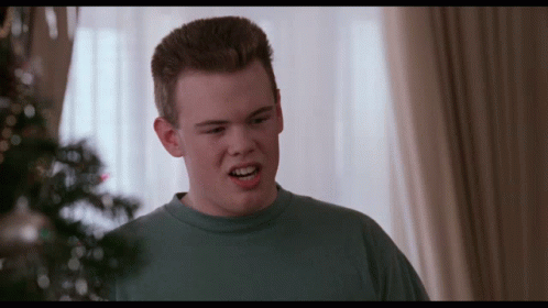 A Young Man In A Blue Shirt Is Making A Face In Front Of A Christmas Tree GIF