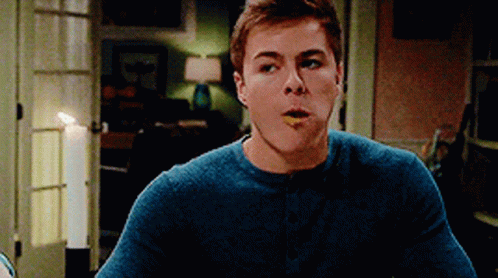 A Young Man In A Blue Sweater Is Eating Something With His Mouth Open GIF