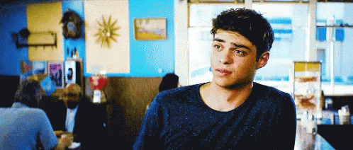 A Young Man In A Blue Sweater Is Sitting At A Table In A Restaurant GIF