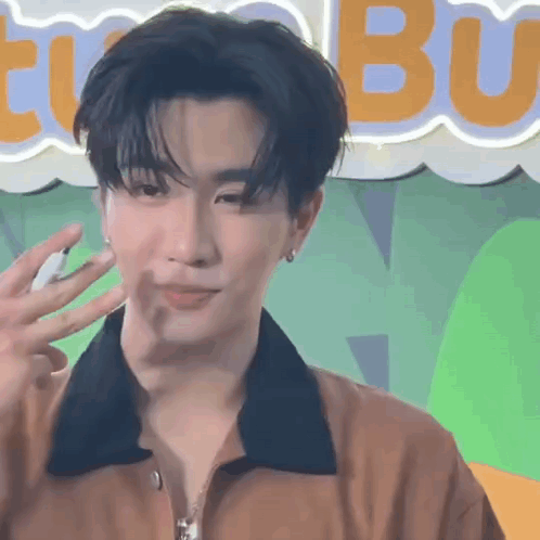 A Young Man In A Brown Jacket Is Waving His Hand In Front Of A Neon Sign . GIF