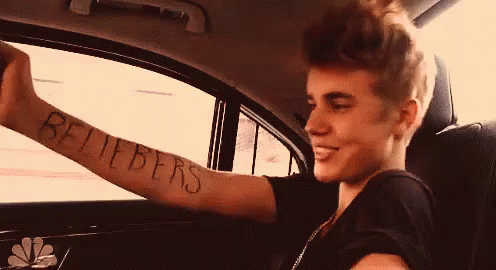 A Young Man In A Car With A Tattoo On His Arm That Says Beliebers GIF