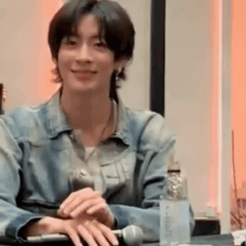 Young Man In Denim Jacket Smiling At Table GIF