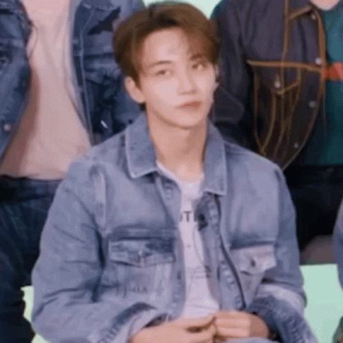 A Young Man In A Denim Jacket Is Sitting In A Group Of People . GIF