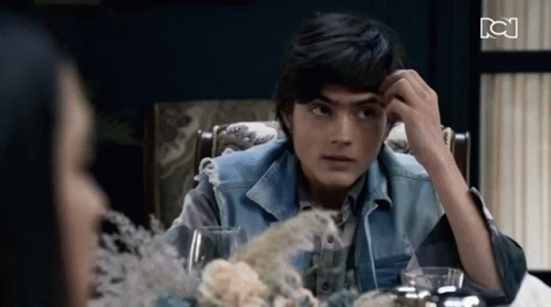 A Young Man In A Denim Vest Sits At A Table With A Woman GIF