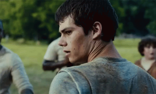A Young Man In A Dirty Shirt Is Standing In A Field Looking At The Camera . GIF