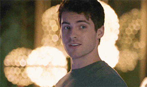A Young Man In A Grey Shirt Looks At The Camera GIF