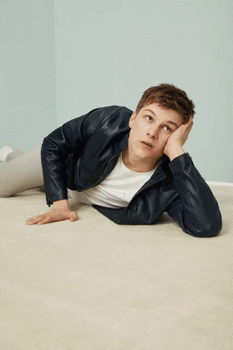 A Young Man In A Leather Jacket Is Laying On The Floor With His Hand On His Face GIF