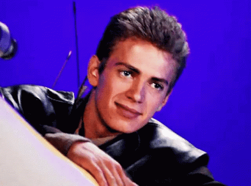 A Young Man In A Leather Jacket Is Leaning On A Table And Smiling . GIF