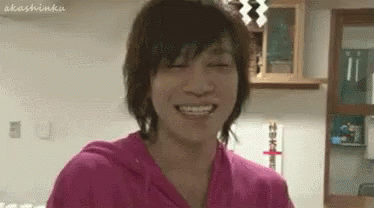 A Young Man In A Pink Shirt Is Smiling With His Eyes Closed In A Room . GIF