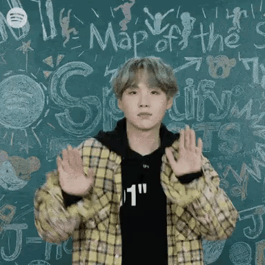 A Young Man In A Plaid Jacket Is Standing In Front Of A Blackboard With His Hands In The Air . GIF