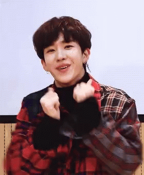 A Young Man In A Plaid Shirt Is Making A Heart Shape With His Hands And Smiling . GIF