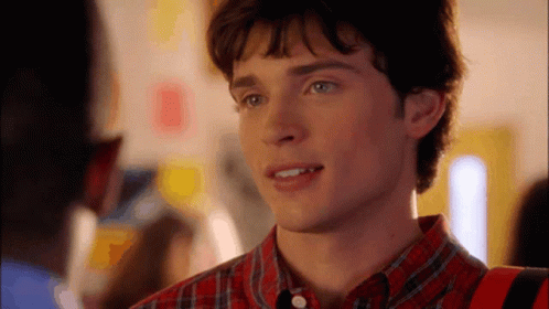 A Young Man In A Plaid Shirt Is Smiling And Looking At Something GIF