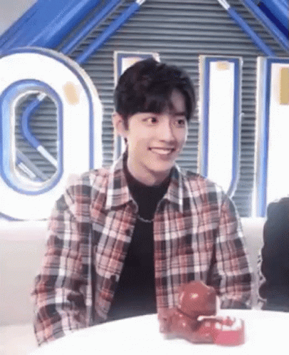 A Young Man In A Plaid Shirt Is Smiling While Sitting At A Table With A Toy On It . GIF
