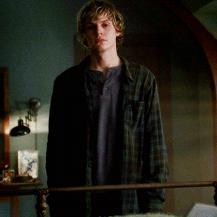 A Young Man In A Plaid Shirt Is Standing Next To A Bed GIF
