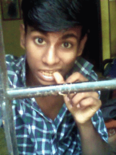 A Young Man In A Plaid Shirt Looks Through A Window GIF
