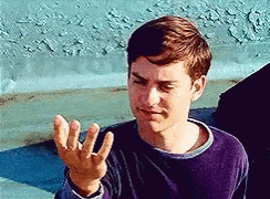 A Young Man In A Purple Shirt Is Making A Funny Face With His Hand . GIF