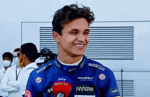 A Young Man In A Racing Suit Is Talking Into A Microphone And Smiling . GIF