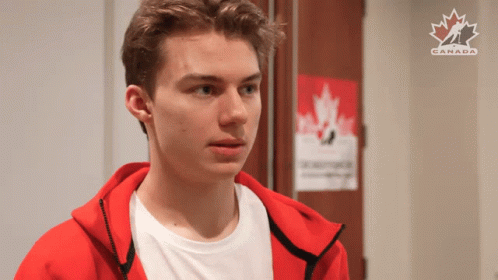 A Young Man In A Red Jacket Is Standing In Front Of A Poster That Says Canada GIF
