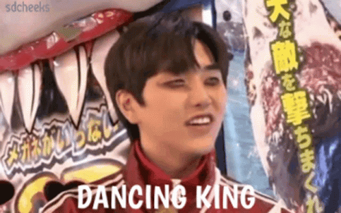 A Young Man In A Red Jacket Is Standing In Front Of A Sign That Says Dancing King . GIF
