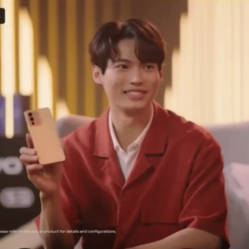 A Young Man In A Red Shirt Is Holding A Cell Phone In His Hand . GIF