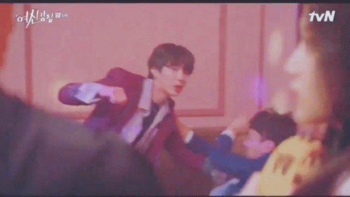 A Young Man In A Red Suit Is Standing In Front Of A Pink Wall And Looking At The Camera . GIF