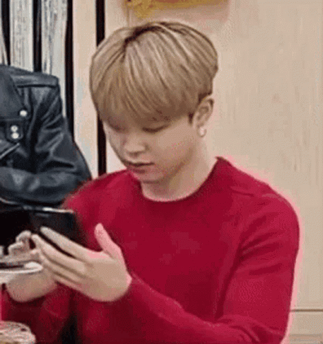 a young man in a red sweater is using a cell phone .