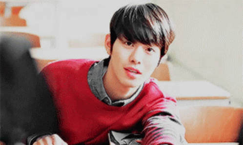 A Young Man In A Red Sweater Sits At A Desk GIF