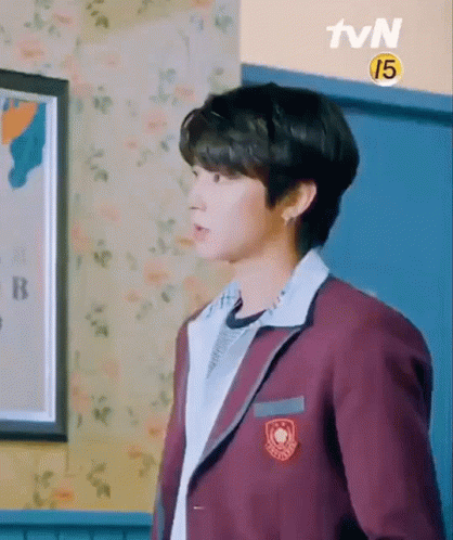 A Young Man In A School Uniform Is Standing In A Room With A Picture On The Wall . GIF