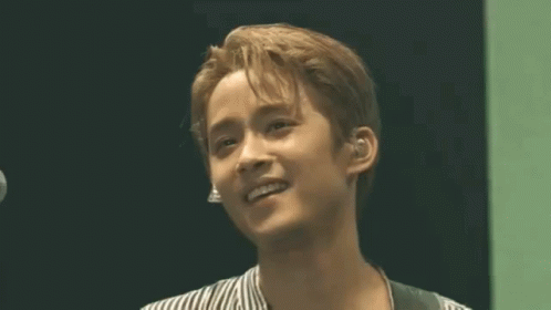A Young Man In A Striped Shirt Is Smiling In Front Of A Microphone GIF