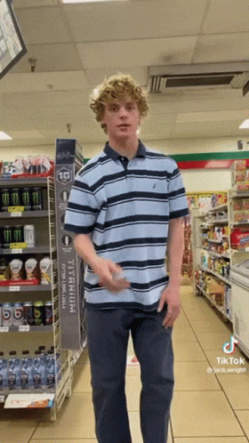 A Young Man In A Striped Shirt Is Standing In A Store GIF