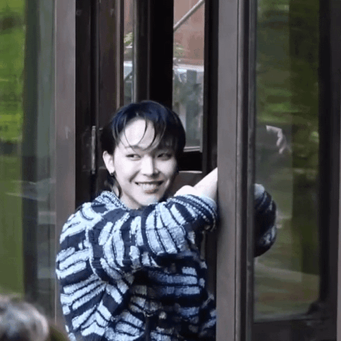A Young Man In A Striped Sweater Is Smiling While Standing In A Doorway . GIF