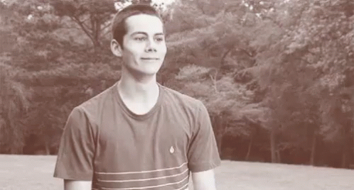A Young Man In A Striped T-Shirt Is Standing In Front Of A Forest . GIF
