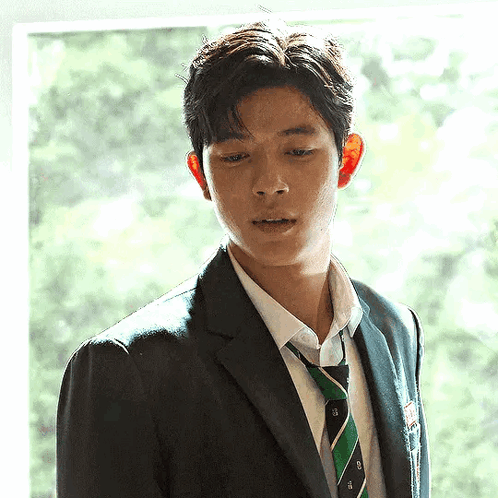A Young Man In A Suit And Tie Is Looking Out Of A Window . GIF