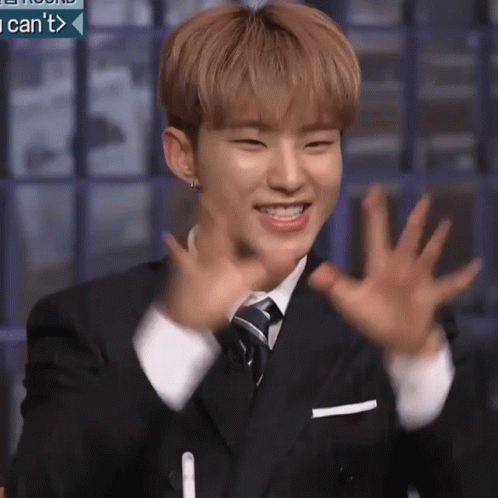 A Young Man In A Suit And Tie Is Smiling And Waving His Hands In The Air . GIF