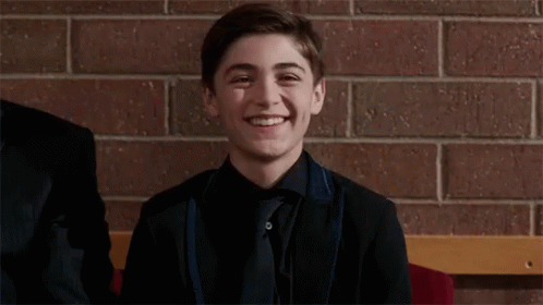 A Young Man In A Suit And Tie Is Smiling While Sitting On A Bench . GIF