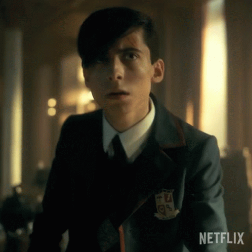 A Young Man In A Suit And Tie Is Standing In A Room Looking At The Camera . GIF