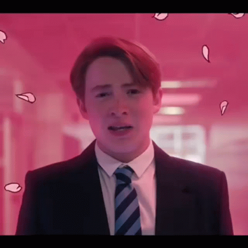 A Young Man In A Suit And Tie Is Standing In Front Of A Pink Wall . GIF