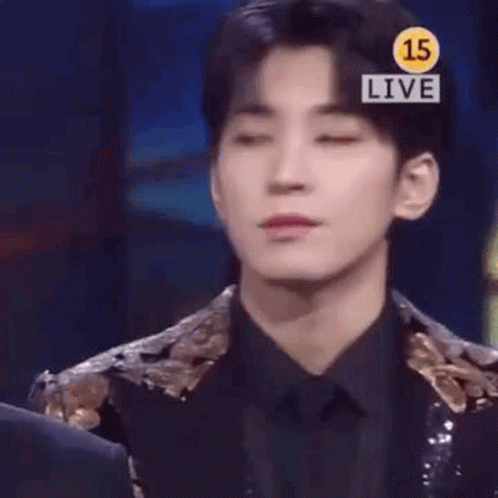 A Young Man In A Suit And Tie Is Standing In Front Of A Sign That Says `` Live '' . GIF