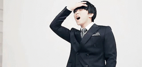 a young man in a suit and tie is yawning while holding his hand to his forehead .
