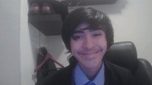 A Young Man In A Suit And Tie Smiles In Front Of A Pair Of Shoes GIF