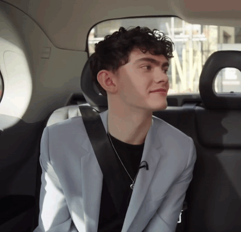 A Young Man In A Suit Is Sitting In The Back Seat Of A Car GIF