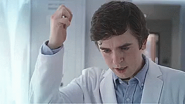 A Young Man In A White Coat Is Holding His Fist Up In The Air . GIF