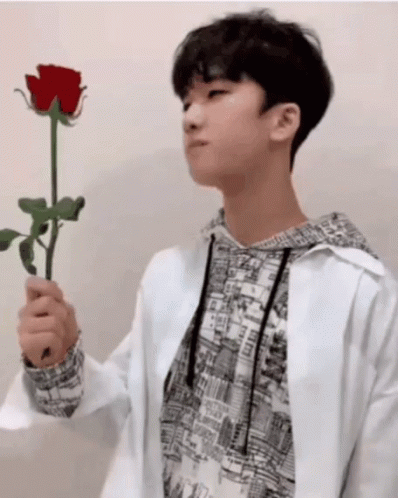 A Young Man In A White Jacket Holds A Red Rose In His Hand GIF
