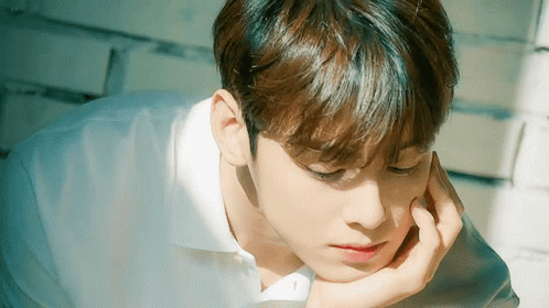 A Young Man In A White Shirt Is Laying Down With His Hand On His Face . GIF