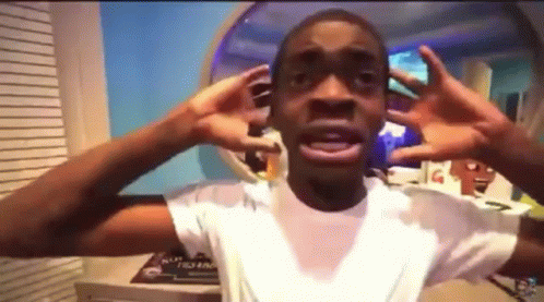 A Young Man In A White Shirt Is Making A Funny Face With His Hands . GIF