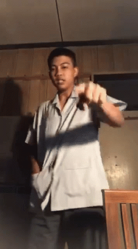 A Young Man In A White Shirt Is Standing In Front Of A Chair GIF